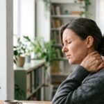 Nackenschmerzen durch Stress: Frau am Schreibtisch hält sich den schmerzenden Nacken